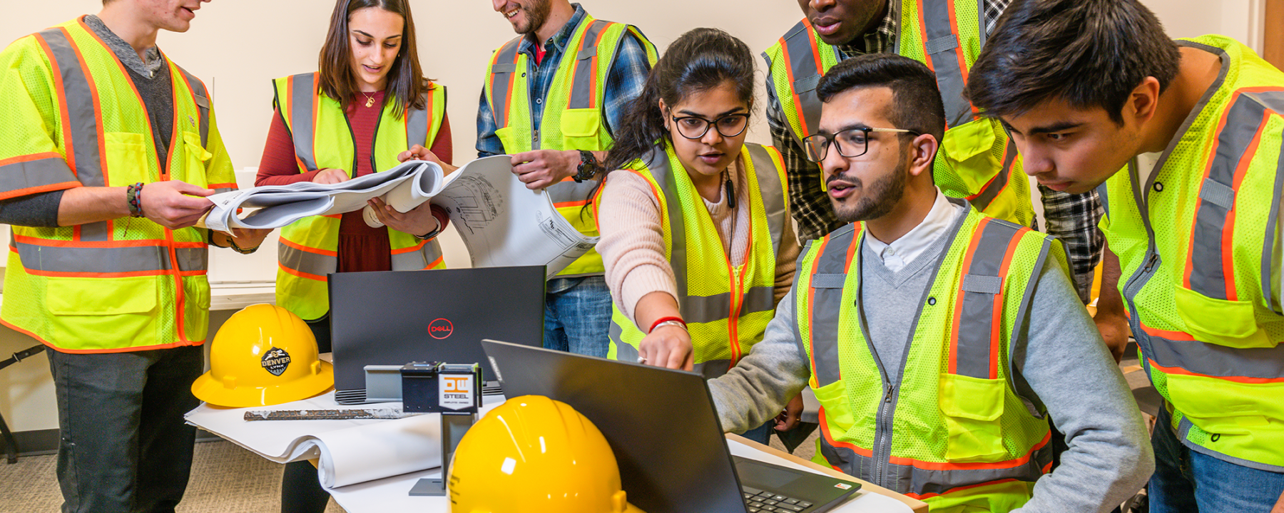Group of CU Denver Civil Engineers and Construction Professionals in hard hats and vests gathered around computers.