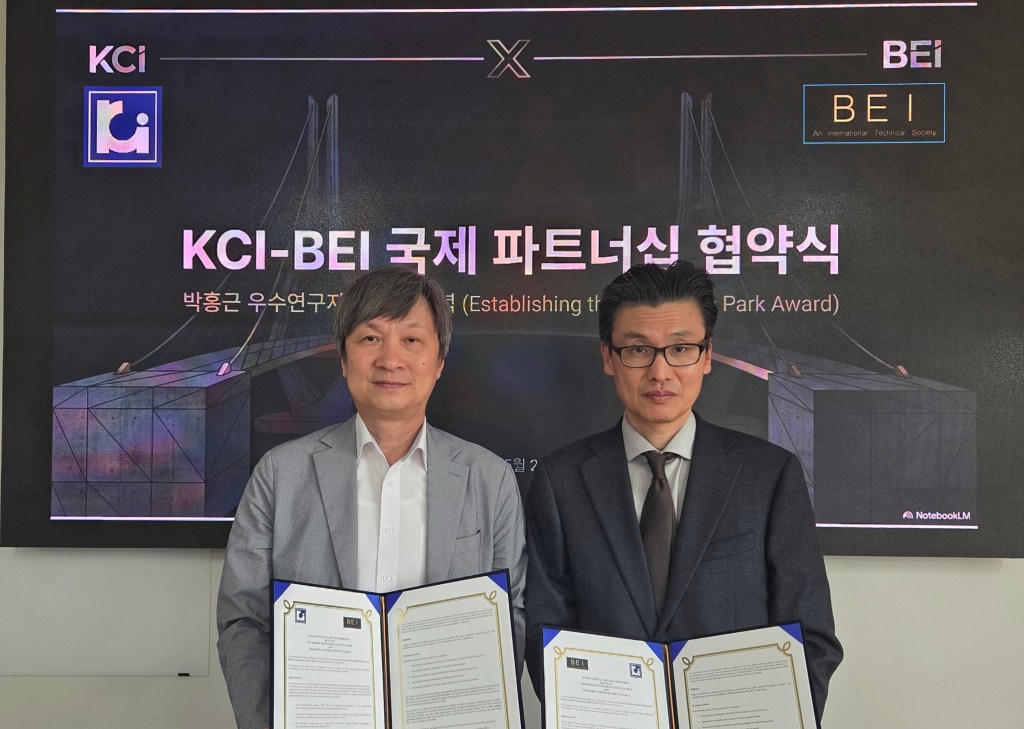Two men in suits, one of them professor Yail Jimmy Kim hold signed partnership documents in front of a screen displaying KCI-BEI international collaboration text in Korean.